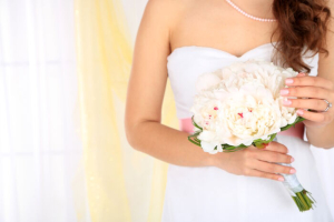 Bride holding wedding bouquet of white peonies, close-up, on light background